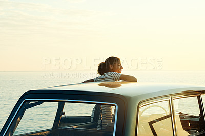 Buy stock photo Shot of a young woman watching the sun go down on a roadtrip