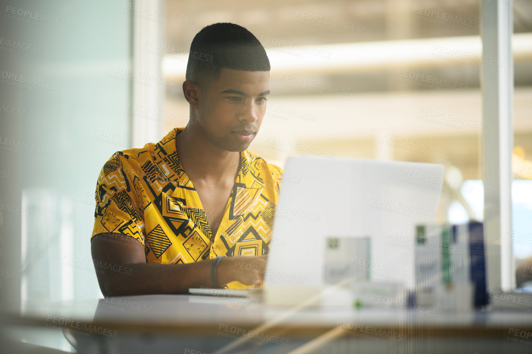 Buy stock photo Shot of a young businessman working on a laptop in an office