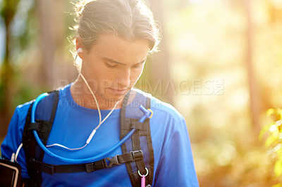 Buy stock photo Fitness, man and earphones with music in forest for hiking podcast, cardio playlist and wellness exercise. Space, hiker and listening to audio with backpack for healthy training, workout and trekking