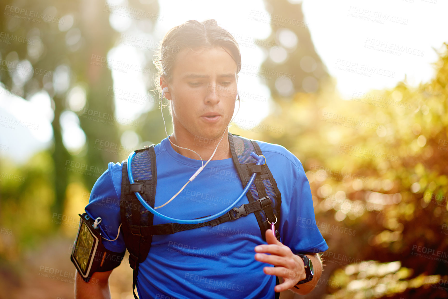 Buy stock photo Earphones, man and running with fitness in forest for marathon training, cardio podcast or breathing exercise. Runner, energy and backpack on mountain trail for sports workout, music or playlist