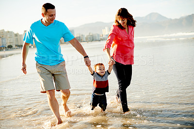 Buy stock photo Beach, holding hands and parents with child in waves for playing, bonding and relax outdoor on holiday. Family, travel and happy dad, mom and kid by ocean for adventure, vacation or weekend in nature