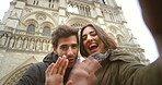 Happy young couple waving during a video call in front of Notre dame