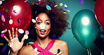 Carefree young woman at a party dancing between colourful balloons and confetti feeling joy. Young woman having fun dancing and shaking her afro at a party. Happy woman dancing between balloons