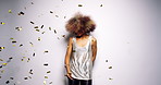 Carefree woman shaking her afro and having fun dancing against a white background at a party while gold confetti falls. Gold confetti falling as happy young African American woman dances