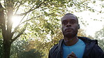 Focused young african american jogging through a park and listening to music on his headphones. Serious young man working out and running through a garden in slow motion listening to music.