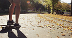 Foot a man skating through a park on his skateboard alone. A man skateboarding on the asphalt through a park on a sunny day. An active man skating through a garden outside