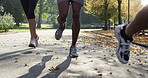 Sport shoes of a diverse group of friends jogging together in the park on the asphalt. A group of fit friends running together through a garden. Friends exercising together in a group outside