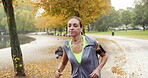 A young woman using her cellphone to listen to music through earphones while jogging through the park. A young woman exercising and running through a garden listening to music in slow motion.