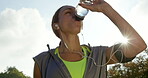 A young woman drinking water from a bottle and listening to music while taking a break during her workout. Young woman working out in the park taking a break to drink water. Young woman drinking water