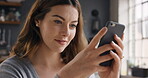 a young woman using a phone at home. A young woman sitting in her kitchen browsing online apps on her cellphone, smiling. A young woman relaxing at home sending a text message on her mobile phone