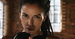 Strong, serious young woman wearing boxing gloves taking a break from her workout in the gym. Portrait of a focused fit woman in boxing gloves ready for a cardio workout. Powerful athlete in the gym