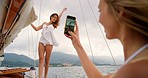 Carefree happy young woman posing on a yacht with a friend taking her photo on a smartphone. Young woman taking a photo of her friend on her cellphone during a holiday cruise on a yacht