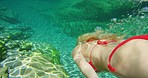 A woman enjoying an underwater swim in her red swimsuit during a summer holiday. A woman on holiday in nature enjoying a swim in a lake. A blonde woman wearing a red bikini swimming in a lake