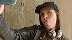 A young woman sticking out her tongue, taking selfies with her cellphone by a wood wall. A happy young student taking selfies on her cellphone. A young woman laughing after looking her selfies