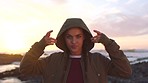 A young woman with pigtails removing her hood enjoying the sunset on the beach. A smiling young woman on holiday removing her hood and enjoying the sunrise.