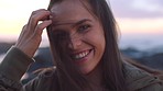 A young woman smiling and removing her hair from her face standing on a windy day while on the promenade. A happy young woman enjoying the sunset on the promenade on a windy day.