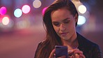 A young woman out in the city at night using her cellphone to send text messages. A woman using her mobile phone to order a taxi at night. A woman looking around using her cellphone at night