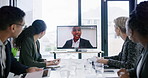 Staff waving to greet happy businessman shown on screen monitor with webcam during virtual teleconference in an office boardroom. Colleagues meeting manage via video call during global webinar online