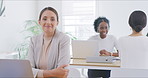 Portrait of businesswoman working on a laptop in a busy office with her colleagues in the background. Focused entrepreneur browsing the internet while planning ideas at her desk in a startup agency