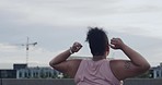 Plus size woman with arms up cheering after her early morning jog. Young curvy female celebrating her fitness milestone. Happy girl in active wear standing with her back, overlooking the city