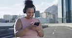 Plus size woman celebrating achieving goal, using cellphone to track weight loss. Chubby active hispanic feeling excited, getting fit, losing fat in routine workout. Listening to music on headphones