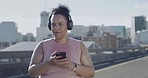 Woman exercising and using a cellphone to track weight loss in city. Chubby active mixed race woman getting fit with a routine outdoor workout. Listening to music on headphones before exercise