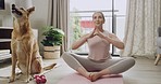 Young calm woman meditating while practicing yoga in a lotus position at home while her dog sits next to her. One fit female meditating and relaxing inside. Focus, relax, find your center and better the health of your body and mind