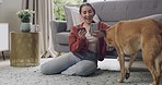 Happy young caucasian woman using cellphone and credit card to do online shopping and banking from device while bonding with pet dog in lounge at home. Carefree woman spending money from smartphone