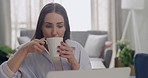 Caucasian remote worker drinking coffee and using laptop for email at home. Young serious woman typing on technology, browsing the internet, searching online. Confident and focused on learning course