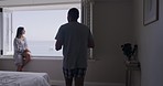 Young and diverse mixed race couple kissing and drinking coffee in a hotel resort while sitting on a window sill with the beach in the background. Handsome young man and his beautiful girlfriend enjoying a morning by the ocean in their pyjamas 