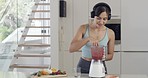 One cheerful fit young mixed race woman tasting a healthy fruit shake  while wearing wireless headphones in the kitchen at home. Drinking fresh fruit juice with vitamins and nutrients to cleanse and provide energy