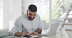 Mixed race businessman smiling and feeling successful with arms folded in home office. Hispanic entrepreneur writing notes in notebook, planning solution and strategy for startup. Using technology