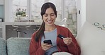 Young cheerful mixed race woman using a phone and credit card and phone at home. Joyful hispanic female cheering with joy while making an online purchase with a debit card and cellphone