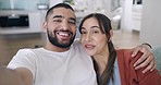 Young mixed race couple relaxing on the sofa in the lounge and taking selfies while laughing and being affectionate. Portrait of a Latin man and woman excited about getting engaged and showing a ring 
