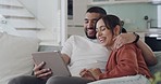 A couple talking on a tablet while sitting on a couch. A young inter racial man and woman video calling together indoors. People waving online.