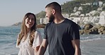 Young happy mixed race couple holding hands and walking on the beach together. Cheerful hispanic boyfriend and girlfriend relaxing at the seaside. Carefree husband and wife spending time at the sea