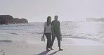 Happy and loving young mixed race couple enjoying a romantic walk at the beach together on a sunny day. Cheerful affectionate boyfriend and girlfriend holding hands while bonding on honeymoon vacation