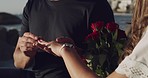  Closeup of a young mixed race male proposing to his girlfriend and putting the ring on her finger while sitting at the beach and sharing an affectionate kiss. Young man smiling as his fiance accepts his wedding proposal while she holds a bunch of roses