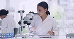 Young female scientists entering sample results into a tablet in a research lab. A science student doing her exam in a laboratory. Woman technician analyzing organisms using a microscope and a device