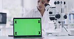 Female scientist analyzing organisms under a microscope and a laptop with a green screen. Woman technician working on research in a lab with modern technology. Biologist looks at sample in laboratory