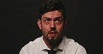 Nervous man looking worried and afraid against black studio background. Scared male being interrogated and looking around worryingly and being fidgety. Male under pressure and acting suspiciously 