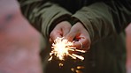 Closeup of woman's hands holding a sparkler and standing alone outside. One playful woman holding a lit bengal light and celebrating an event. Playing with sparkles or sparkly fireworks and having fun