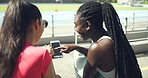Female athletes laughing while using phone and browsing online together after exercise at stadium. Sporty friends and teammates resting after fitness training and using social media at sports ground