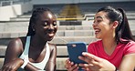 Two athletes listening to music on phone and dancing after a workout training session in a sports stadium. Fit, active, sporty and athletic young women bonding during a break from exercise in arena