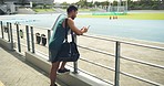 Young male athlete waiting for his training coach while texting on his phone to pass the time. Sports man looking at his smartwatch on his break and preparing for a practice workout near sports field