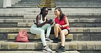 Two female athletes using a phone and talking after a workout in sports stadium. Fit, young man sitting down with friends after training. Team of active and sporty athletes bonding after exercise