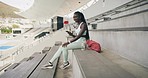 African female athlete checking notifications on her phone while sitting in a stadium. Active woman wearing sportswear typing on a cellphone. Sportswoman updating social media after exercising