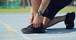 Closeup of runner tying shoe laces before running on an athletics track. Active athlete wearing a fitness tracker watch on a sports arena. Sports person tying shoestring before jogging and training