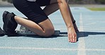 Active fit athlete at a starting line to run a race in sportswear. Crouched, ready to start sprinting on a track. Female practicing a cardio workout in a stadium to increase speed and stamina