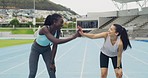 Two sporty women giving high five after a run and checking progress on smartwatch. Young athletes exercising on tracks and feeling confident after finishing a workout. Fitness friends congratulating
